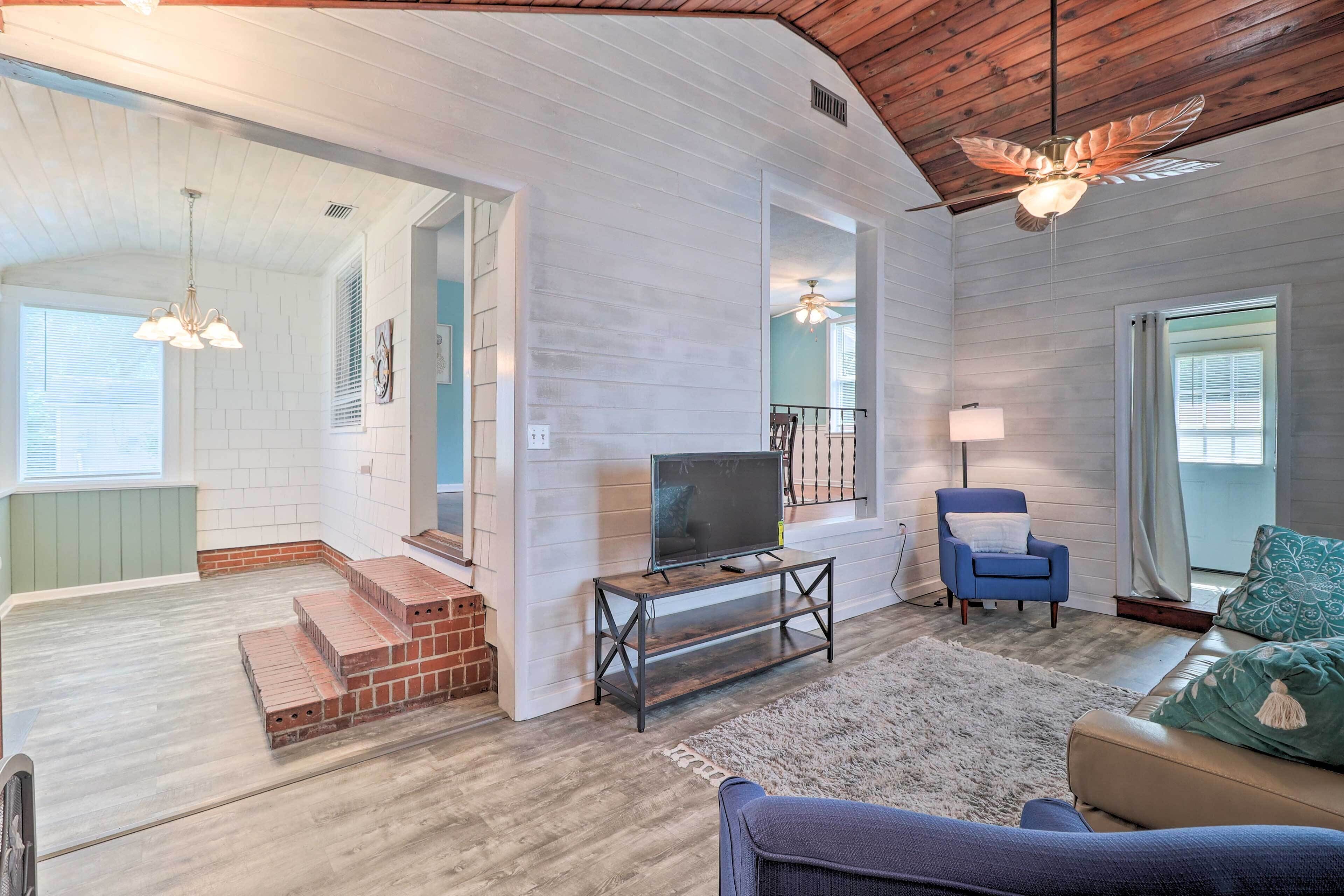 A spacious living area with a TV on a wooden stand, a blue armchair, and a beige sofa.