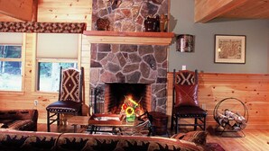 A cozy cabin interior with a stone fireplace, wooden walls, and a comfortable seating area. - Upscale Fryeburg Cabin: Hot Tub + Billiards Table! (Fryeburg)