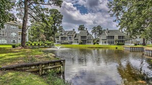 A large, multi-story building with a pond in front, surrounded by trees and a well-maintained lawn. - Lovely Myrtle Beach Condo: 4 Mi to Boardwalk! (Myrtle Beach)