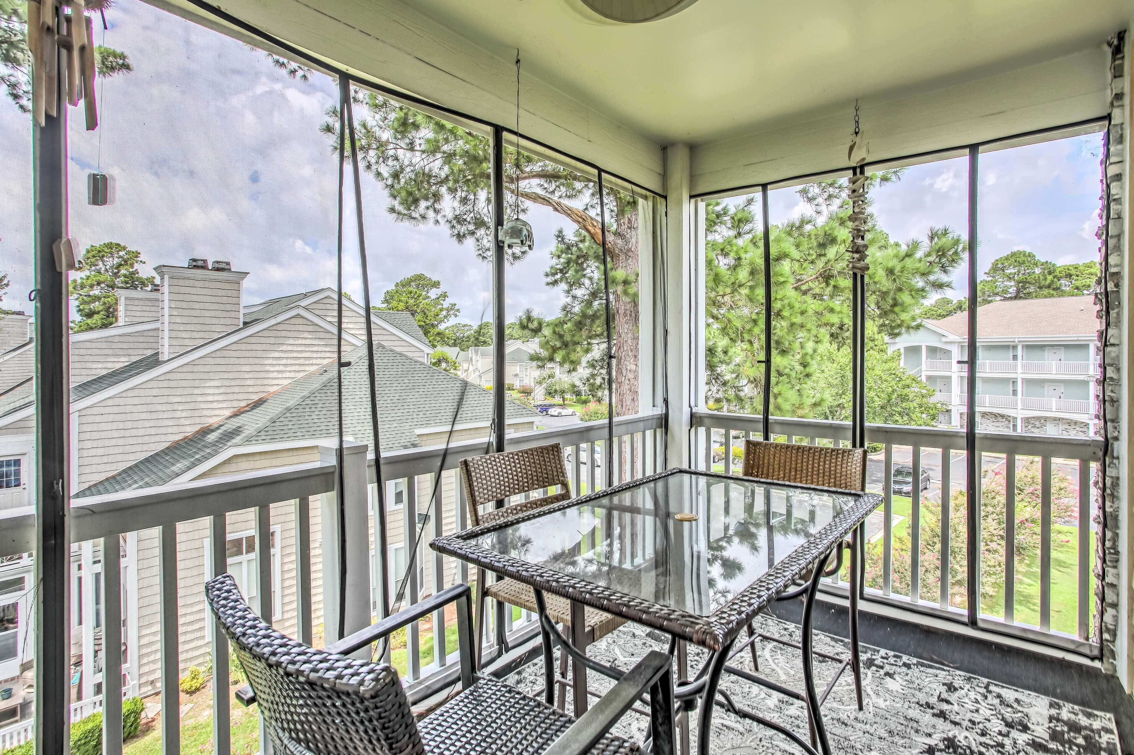 A covered patio with a glass table and wicker chairs, overlooking a residential neighborhood.