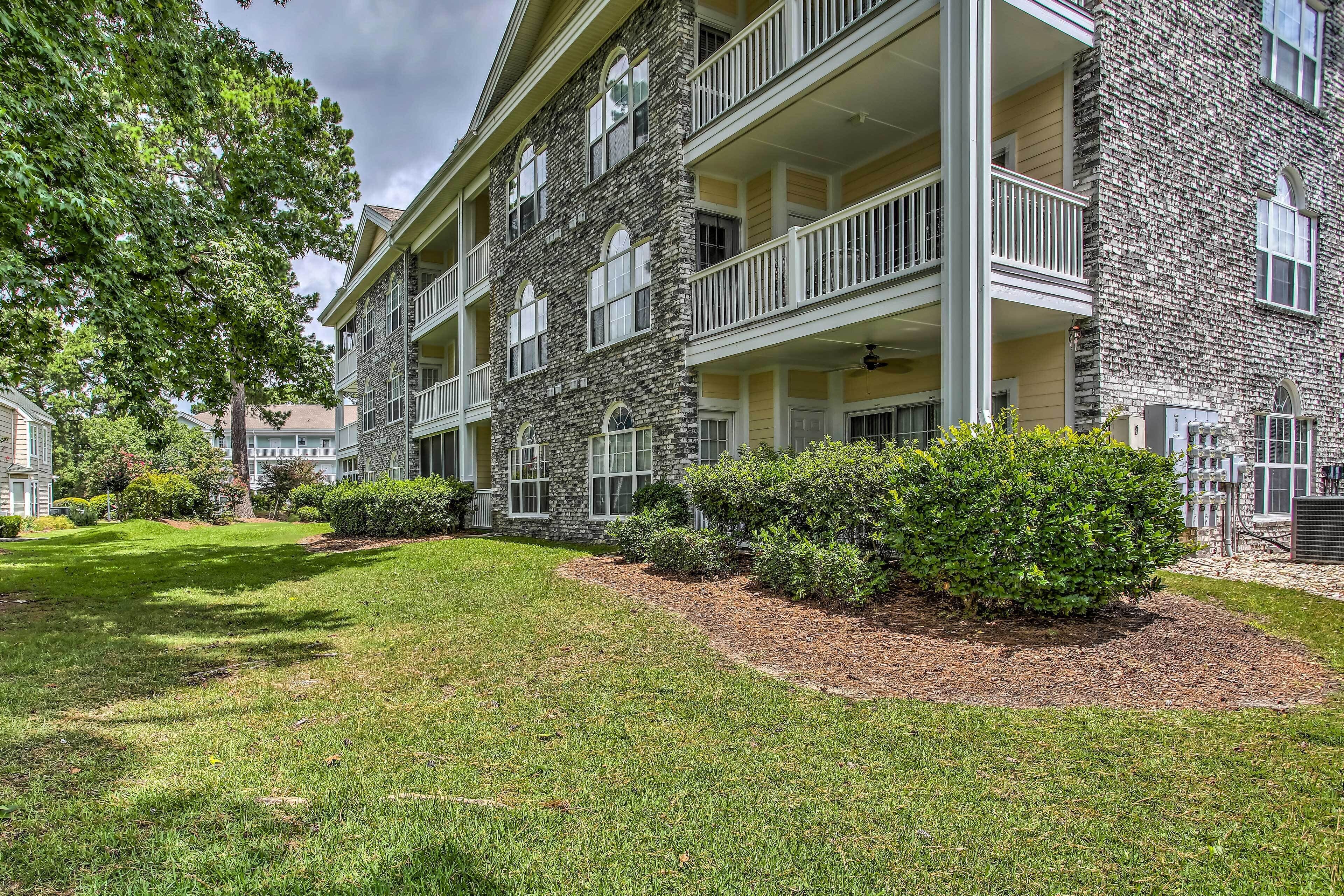 A multi-story building with stone facade, balconies, and a well-maintained lawn.