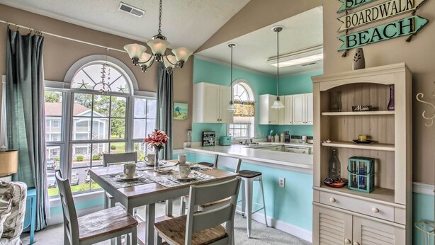 A dining area with a table and chairs, a kitchen with white cabinets, and a sign that reads 'BOARDWALK BEACH'. - Lovely Myrtle Beach Condo: 4 Mi to Boardwalk! (Myrtle Beach)