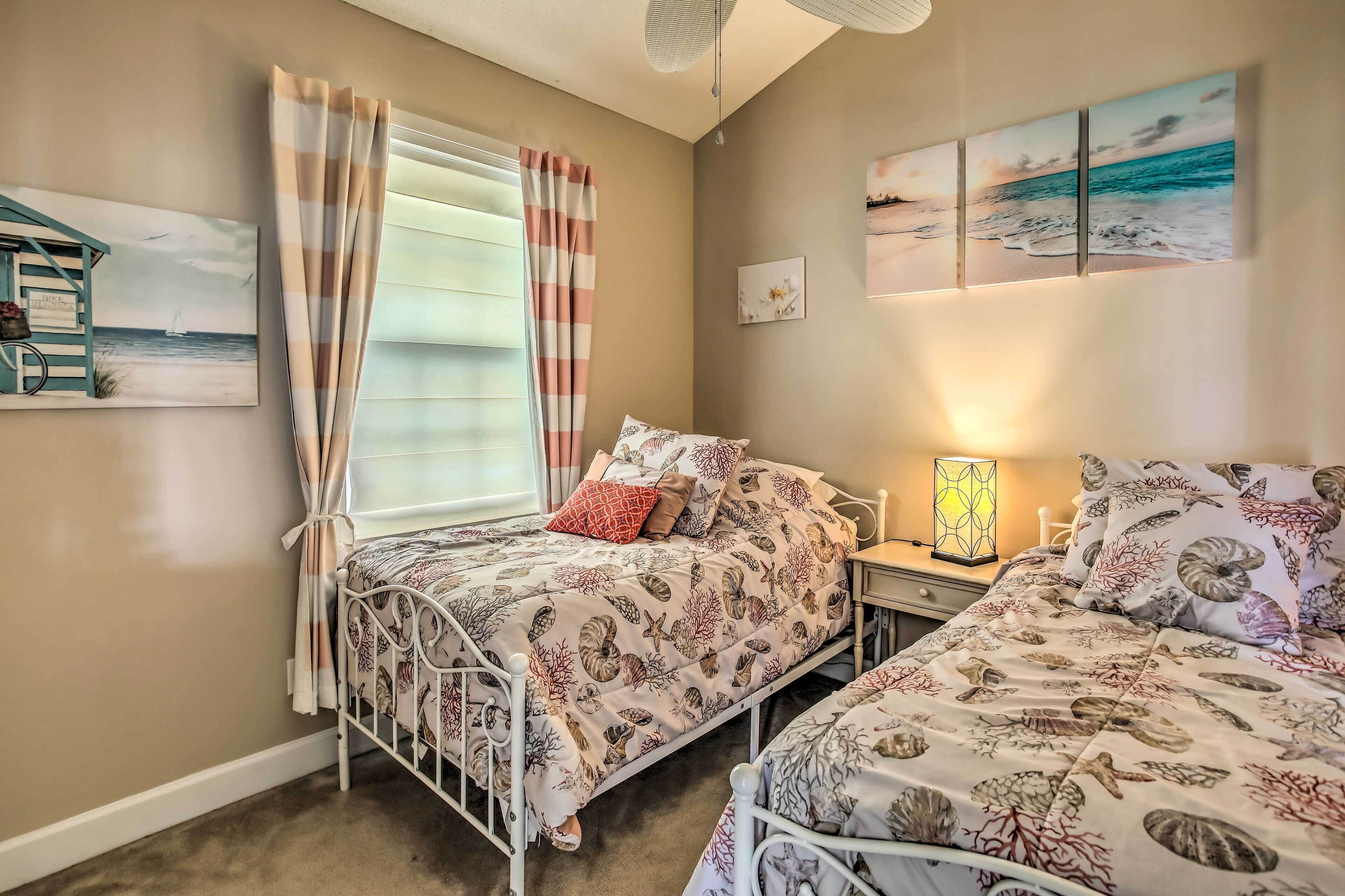 Un dormitorio con dos camas, una ventana con cortinas, una mesita de noche con lámpara y decoración en la pared.