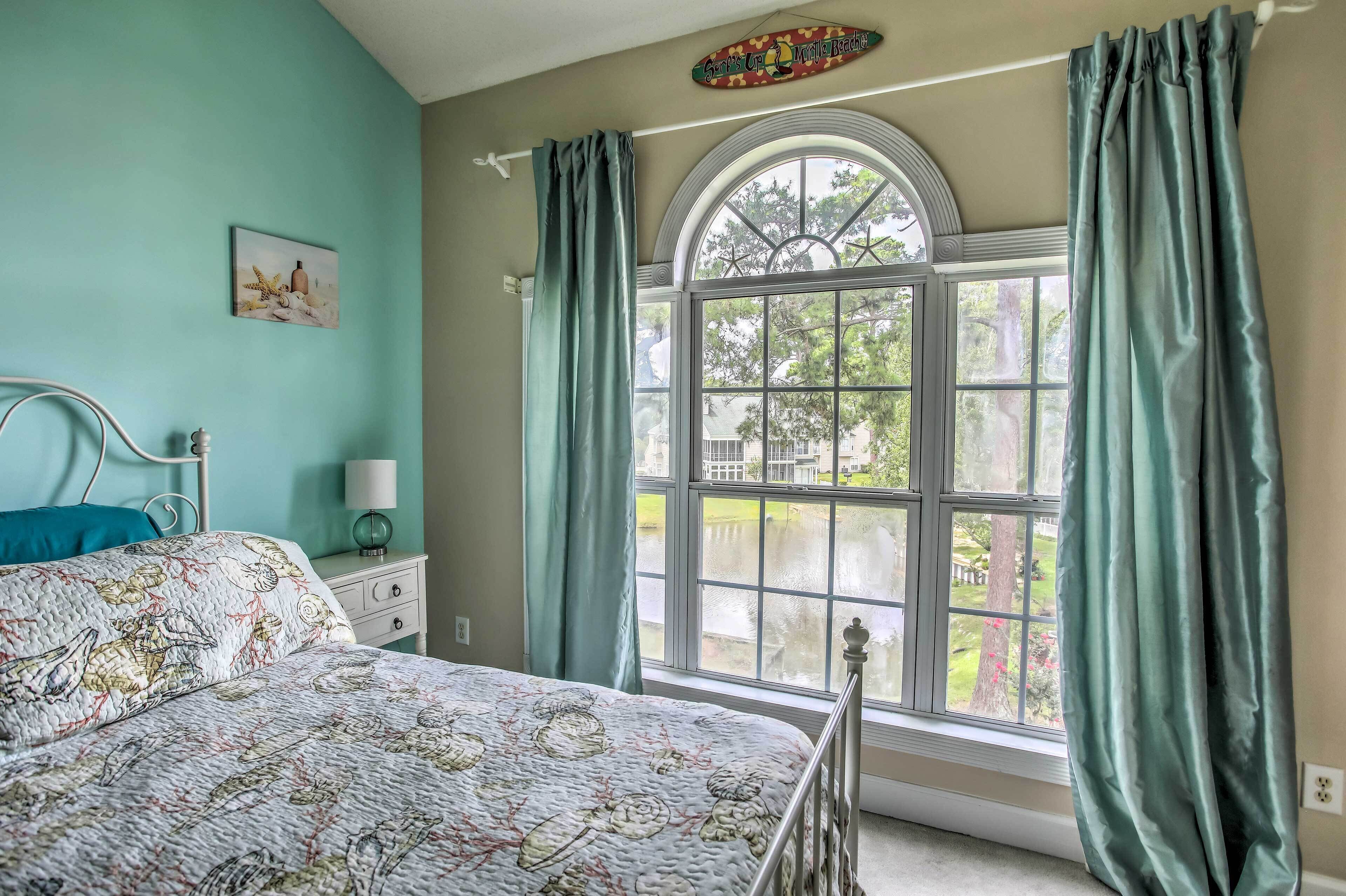 A bedroom with a bed, a nightstand, a lamp, and a window with curtains.