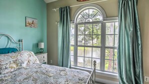 A bedroom with a bed, a nightstand, a lamp, and a window with curtains. - Lovely Myrtle Beach Condo: 4 Mi to Boardwalk! (Myrtle Beach)