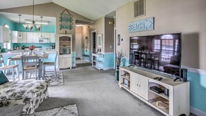 A modern kitchen with white cabinets, a dining area with a table and chairs, a living room with a TV and entertainment unit, and a hallway leading to bedrooms. - Lovely Myrtle Beach Condo: 4 Mi to Boardwalk! (Myrtle Beach)