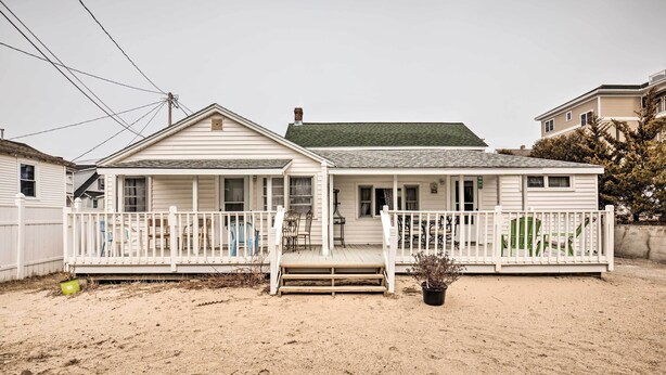A two-story house with a porch, a small garden, and a sandy yard. - Cozy Hampton Cottage w/ BBQ - Walk to Ocean! (Hampton)
