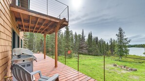 A wooden deck with a grill and chairs, overlooking a grassy area and a lake. - Spacious Soldotna Home w/ Mackey Lake Views! (Soldotna)