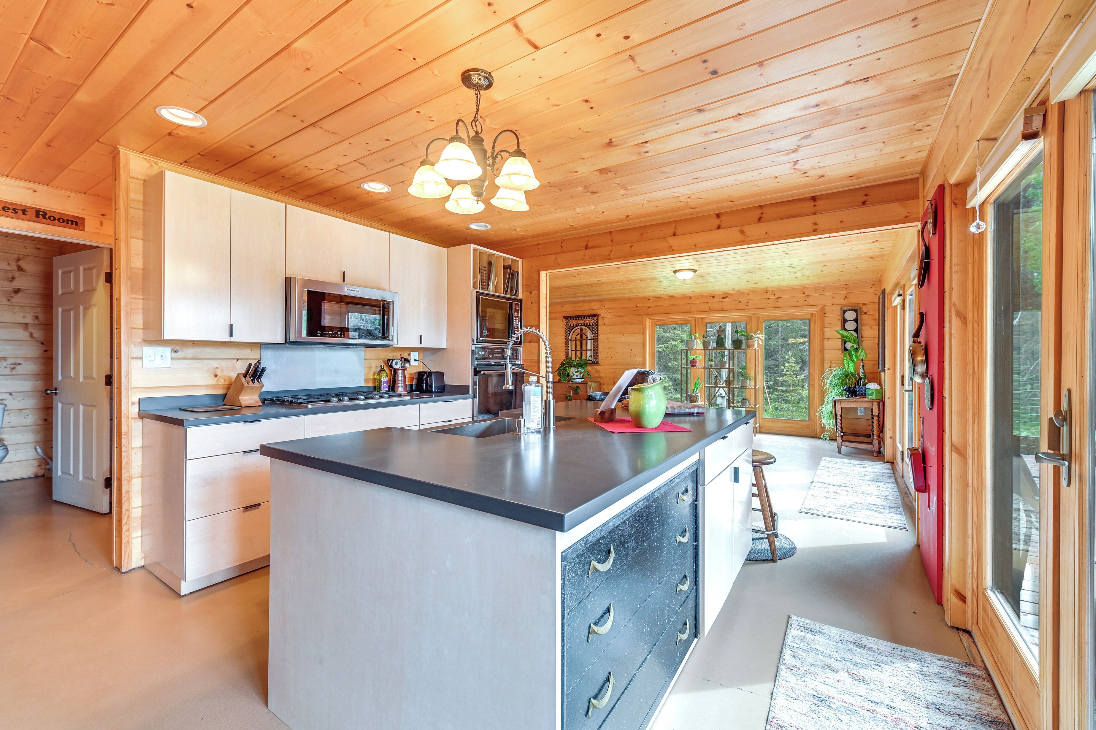 A modern kitchen with wooden ceilings, a central island, and a view of the outdoors.