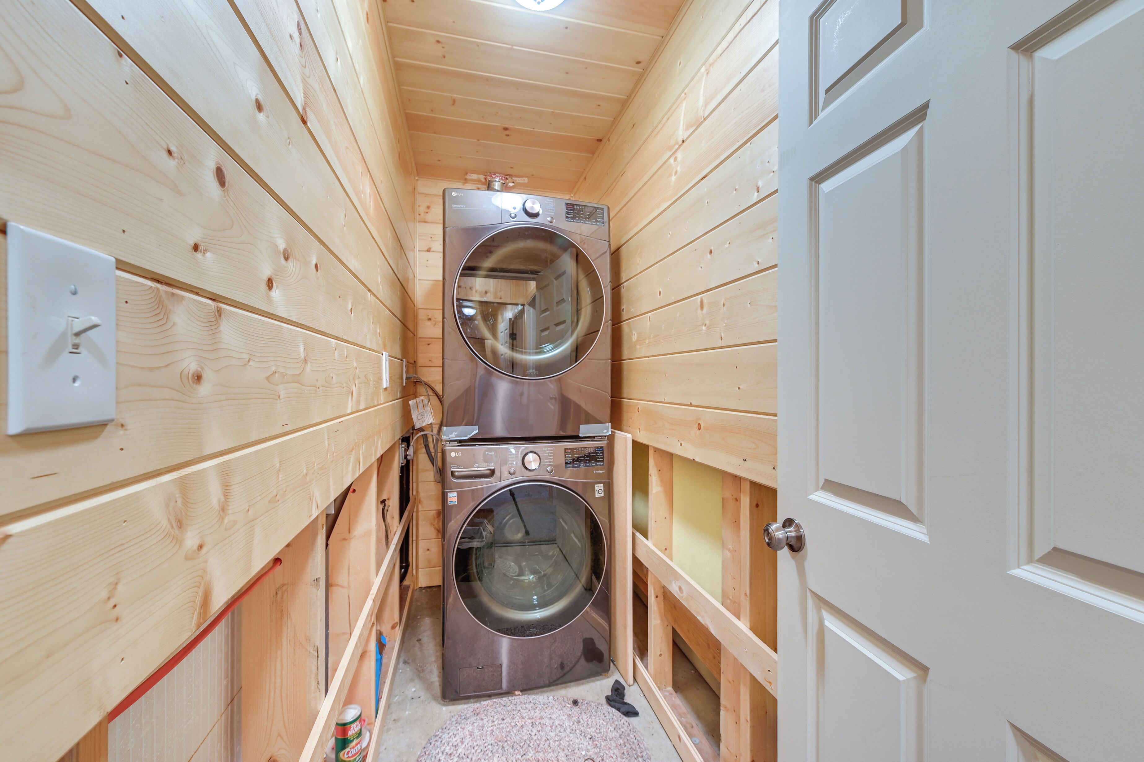 A narrow wooden room with two stacked washing machines and a door.