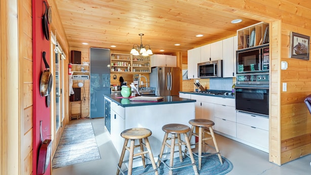 A modern kitchen with wooden cabinets, stainless steel appliances, and a central island with stools. - Spacious Soldotna Home w/ Mackey Lake Views! (Soldotna)