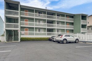 A multi-story building with balconies, a parking lot, and a gated entrance.