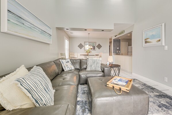 A modern living room with a sectional sofa, a coffee table, and a dining area in the background.