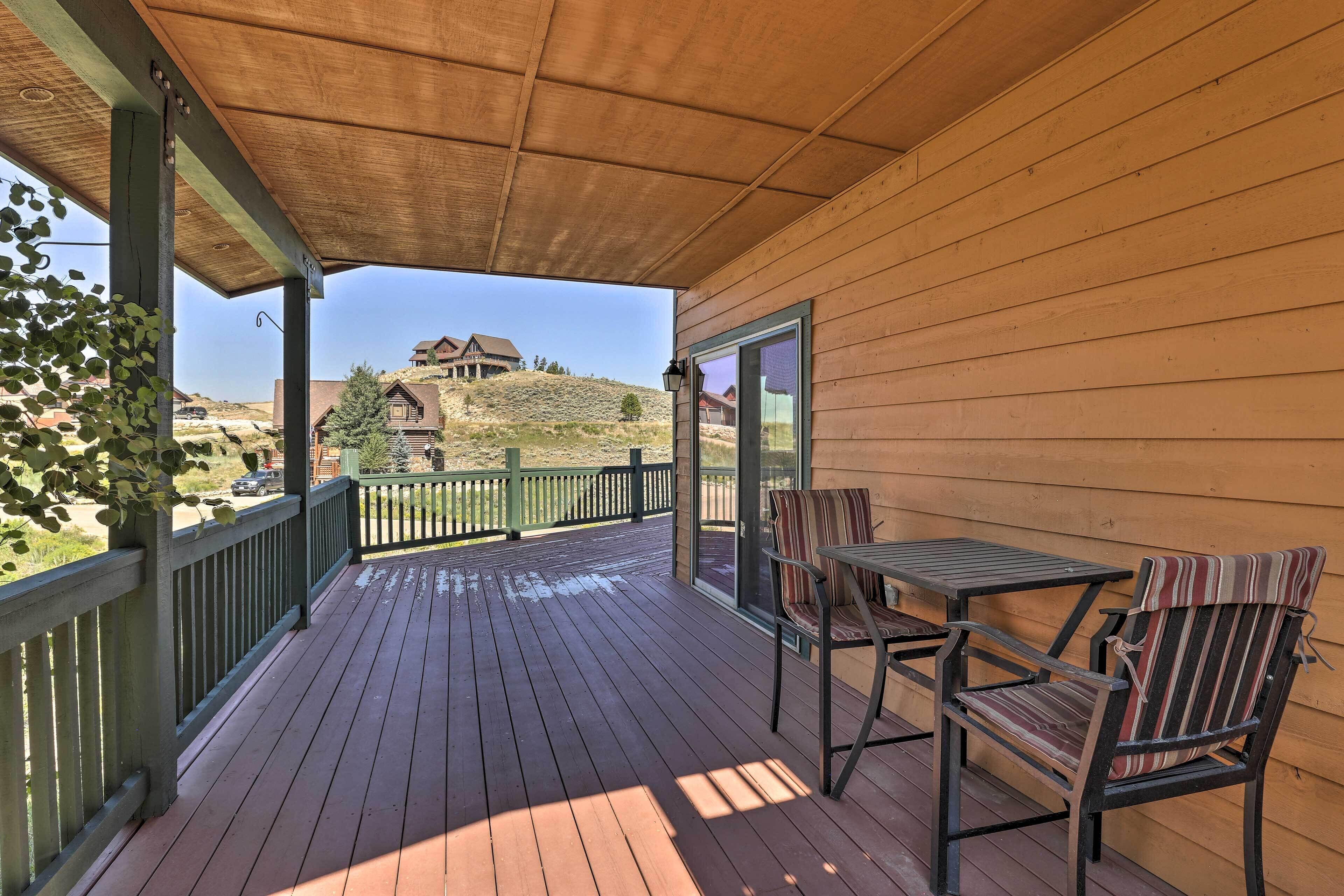 A wooden deck with a table and chairs, overlooking a hill with a house.