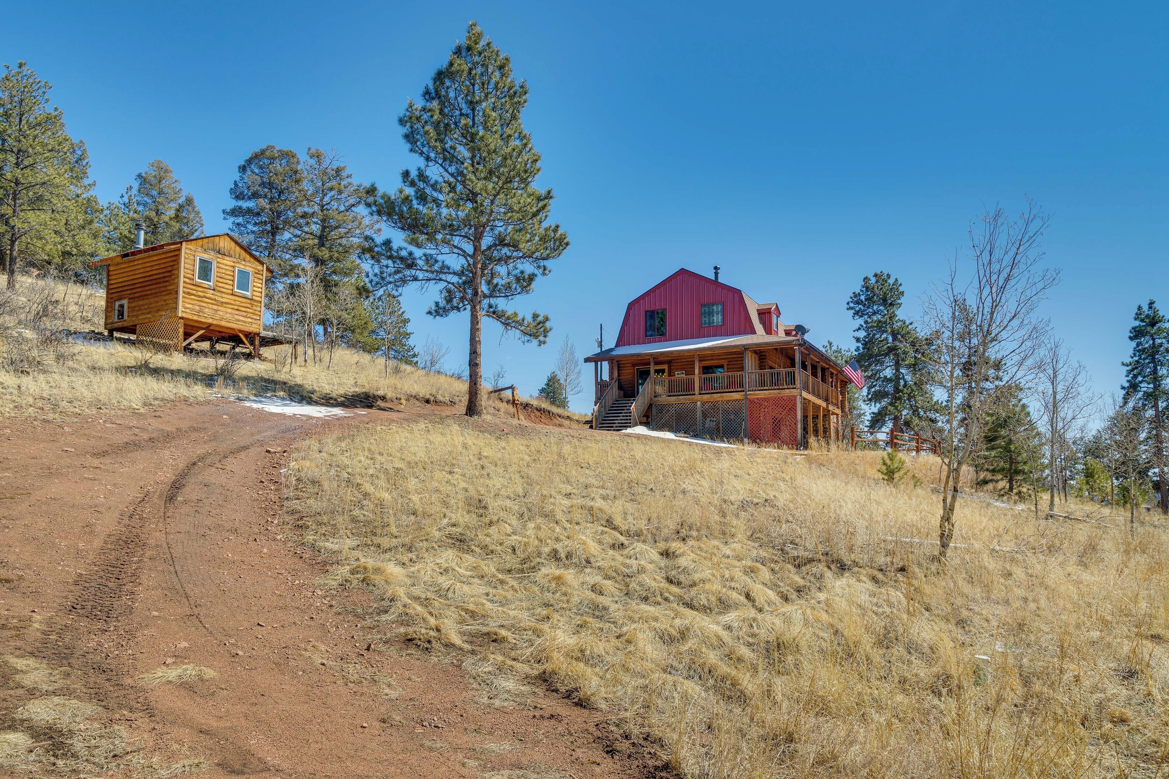 A rustic cabin and a large house on a hillside with a dirt path leading to the cabin.