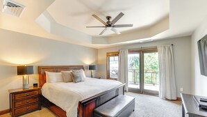 A bedroom with a large bed, a wooden nightstand, a bench, a ceiling fan, a desk, and a window with curtains. - Half-mi to Payette Lake: Dtwn Mccall Condo! (McCall)
