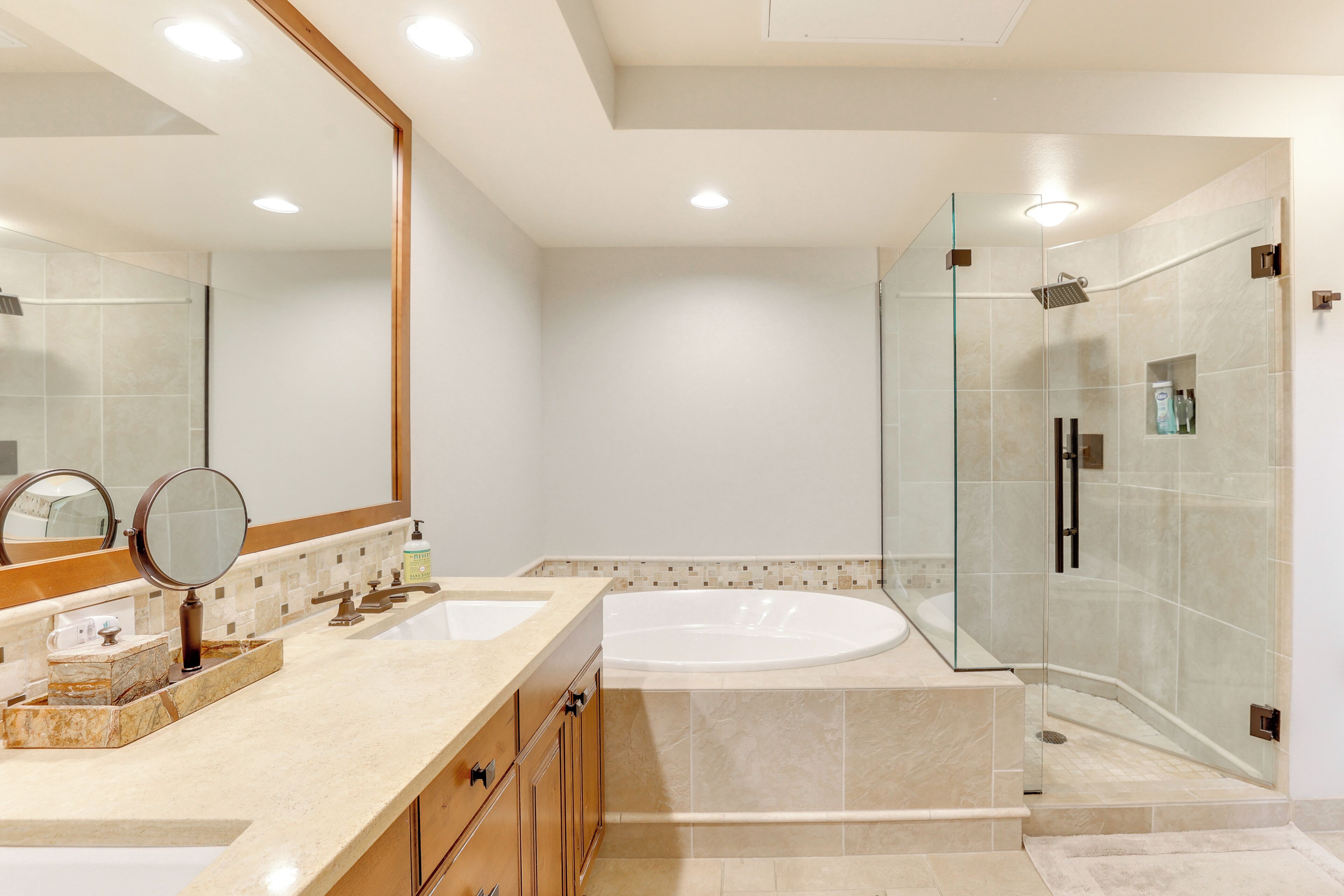 A modern bathroom with a large mirror, two sinks, a bathtub, and a glass-enclosed shower area.