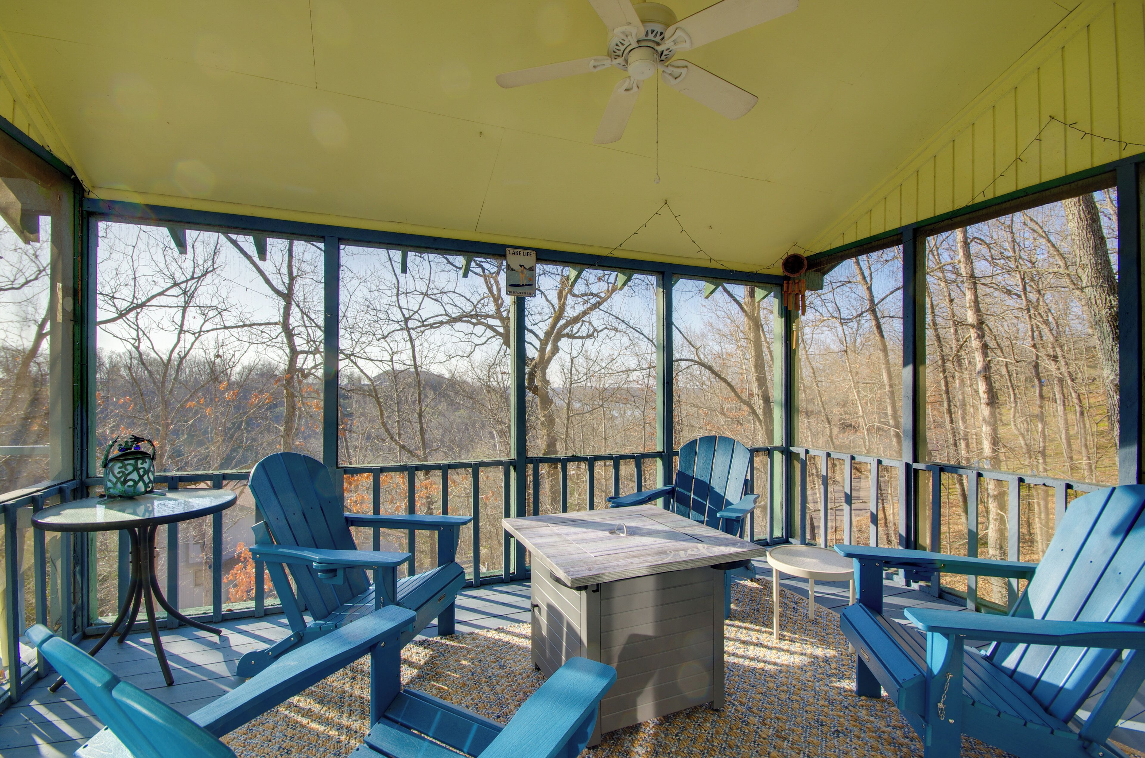 A covered outdoor seating area with Adirondack chairs, a table, and a ceiling fan.