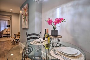 A dining area with a glass table, chairs, a wine bottle, and a vase with pink flowers. - Charming Apt W/patio: Walk to Downtown Albany (Albany)