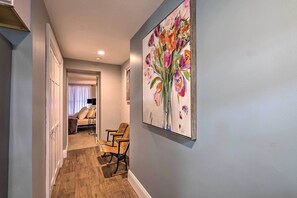 A hallway with wooden flooring, a painting of flowers on the wall, and a seating area with chairs and a sofa. - Charming Apt W/patio: Walk to Downtown Albany (Albany)