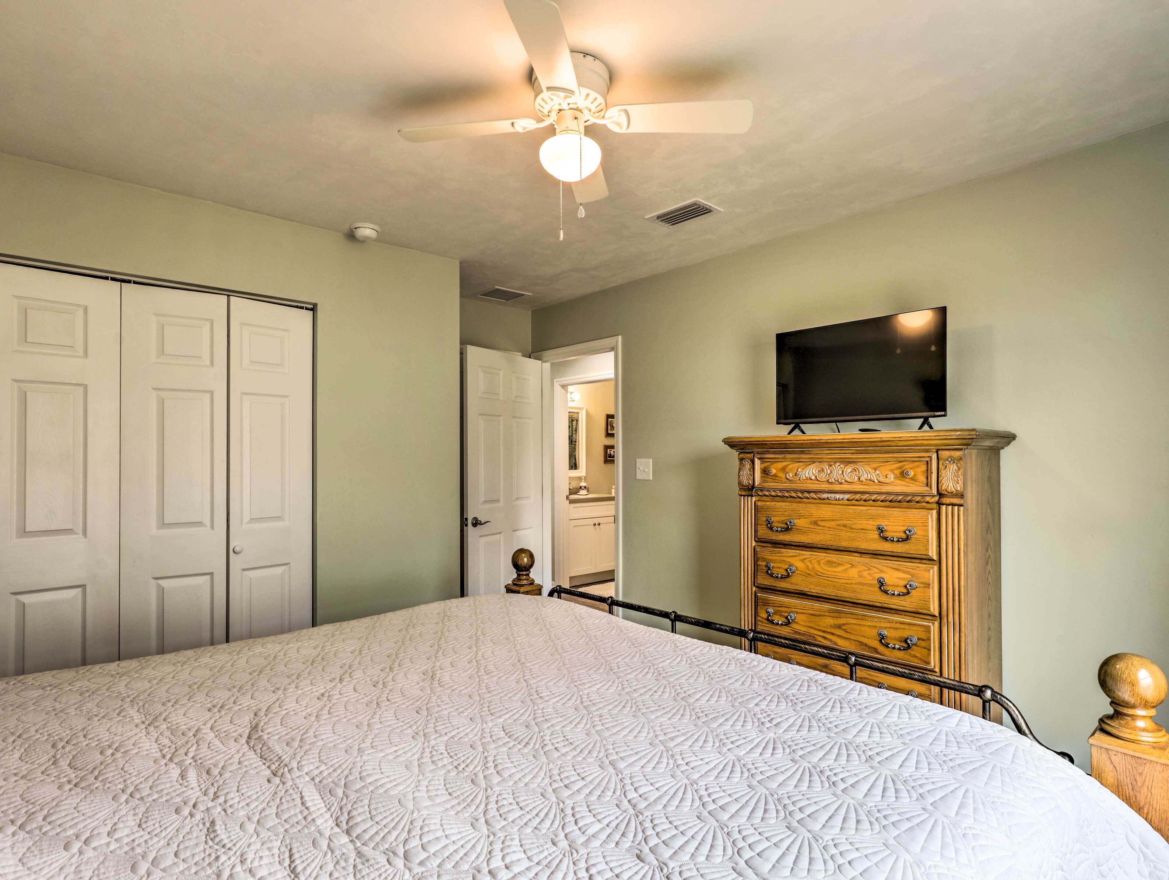 Een slaapkamer met een groot bed, een houten dressoir, een plafondventilator en een televisie aan de muur.