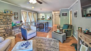 A living room with a stone fireplace, a ceiling fan, and a dining area with a kitchen in the background. - Mount Ida Condo w/ Balcony + Resort Amenities (Mount Ida)