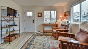 A cozy living room with a wooden floor, a patterned rug, a TV on a metal shelf, a desk with a lamp, and a chair with a fur throw. - Goldendale Vacation Rental 13 Mi to Columbia River (Goldendale)