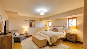 Quarto com cama, mesas de cabeceira, escrivaninha, cadeira e televisão.