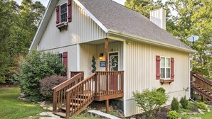 A two-story house with a porch, wooden staircase, and a satellite dish. - Hot Tub & Wooded Views: Lakefront Blue Eye Cottage (Blue Eye)