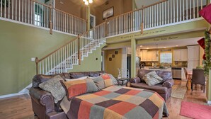 A spacious living area with a large sectional sofa, a staircase, and a view of the kitchen. - Hot Tub & Wooded Views: Lakefront Blue Eye Cottage (Blue Eye)