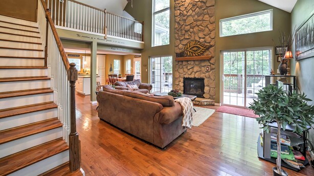 A spacious living area with a large brown sofa, a fireplace, and a stone accent wall. - Hot Tub & Wooded Views: Lakefront Blue Eye Cottage (Blue Eye)