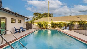 A swimming pool with a ladder, two blue chairs, and a fence. - Retro St Pete Home w/ Private Heated Pool (St. Petersburg)
