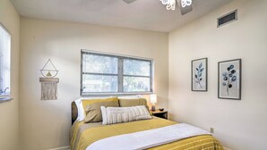 A bedroom with a bed, a window, a wall-mounted lamp, and two framed pictures. - Retro St Pete Home w/ Private Heated Pool (St. Petersburg)