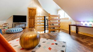 A cozy attic room with a sloped ceiling, a television, a wooden ladder, and a colorful rug. - Lakeside Indiana Vacation Rental Near Fort Wayne! (Churubusco)