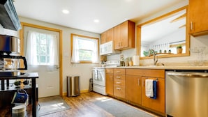 A modern kitchen with wooden cabinets, stainless steel appliances, and a window with curtains. - Lakeside Indiana Vacation Rental Near Fort Wayne! (Churubusco)