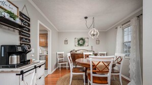 A dining area with a round wooden table, white chairs, a coffee station, and a chandelier. - Single-story Manchester Home Close to Parks! (Manchester)