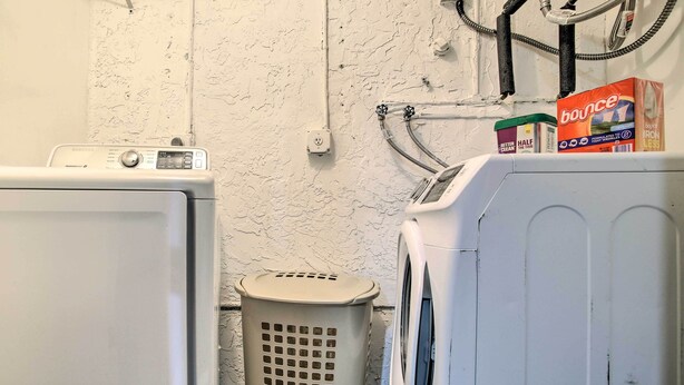 A laundry area with a washing machine, dryer, and a laundry basket. - Lovely Lauderhill Retreat < 12 Mi to Beach! (Lauderhill)