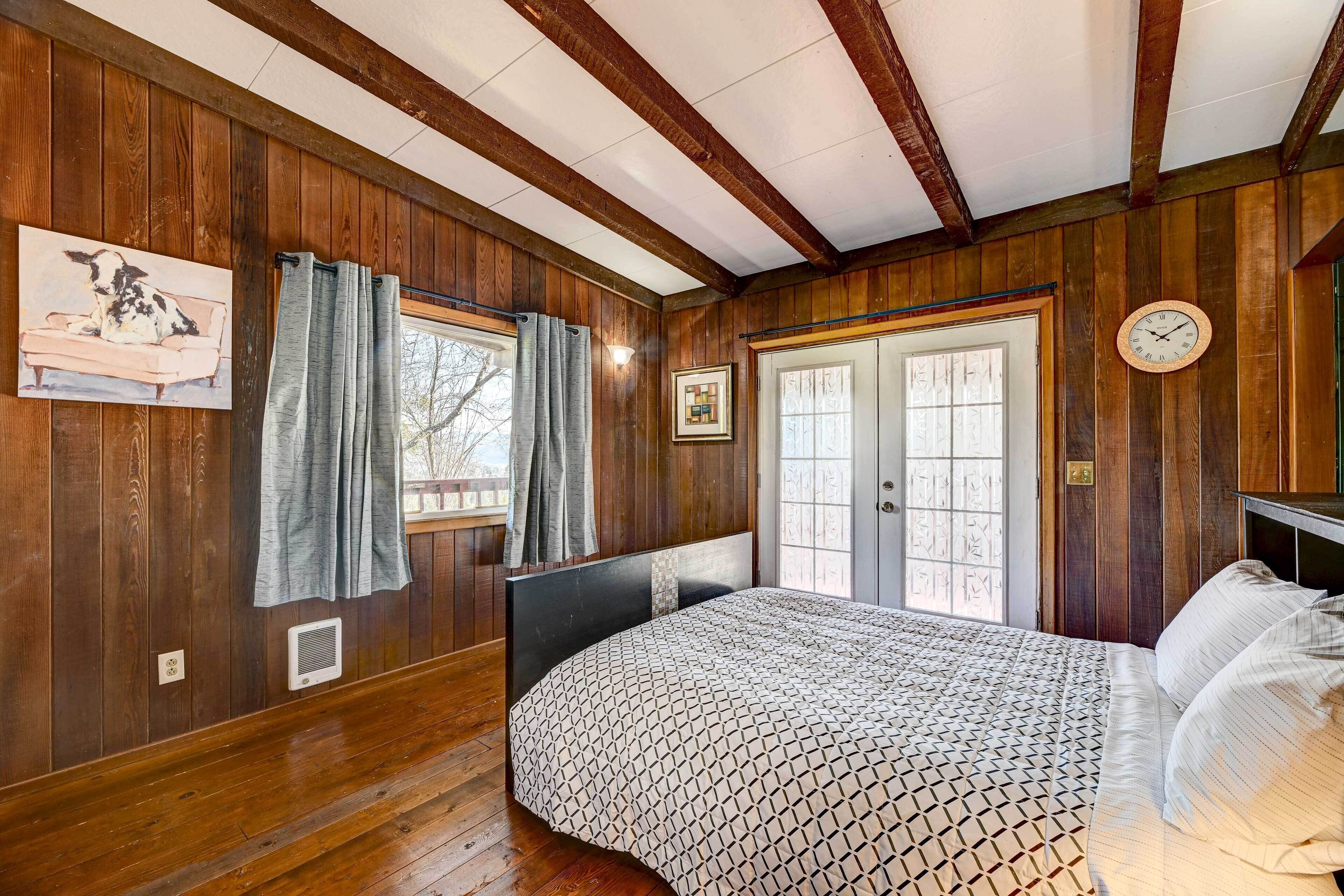 Une chambre à coucher aux murs lambrés, avec un lit, deux portes, une horloge et une fenêtre avec des rideaux.