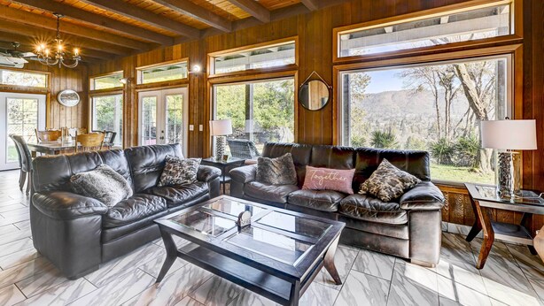 A spacious living room with leather sofas, a glass coffee table, and large windows offering a view of the outdoors.