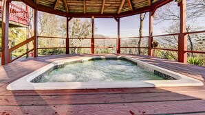 A hot tub under a wooden gazebo with a view of trees and hills.