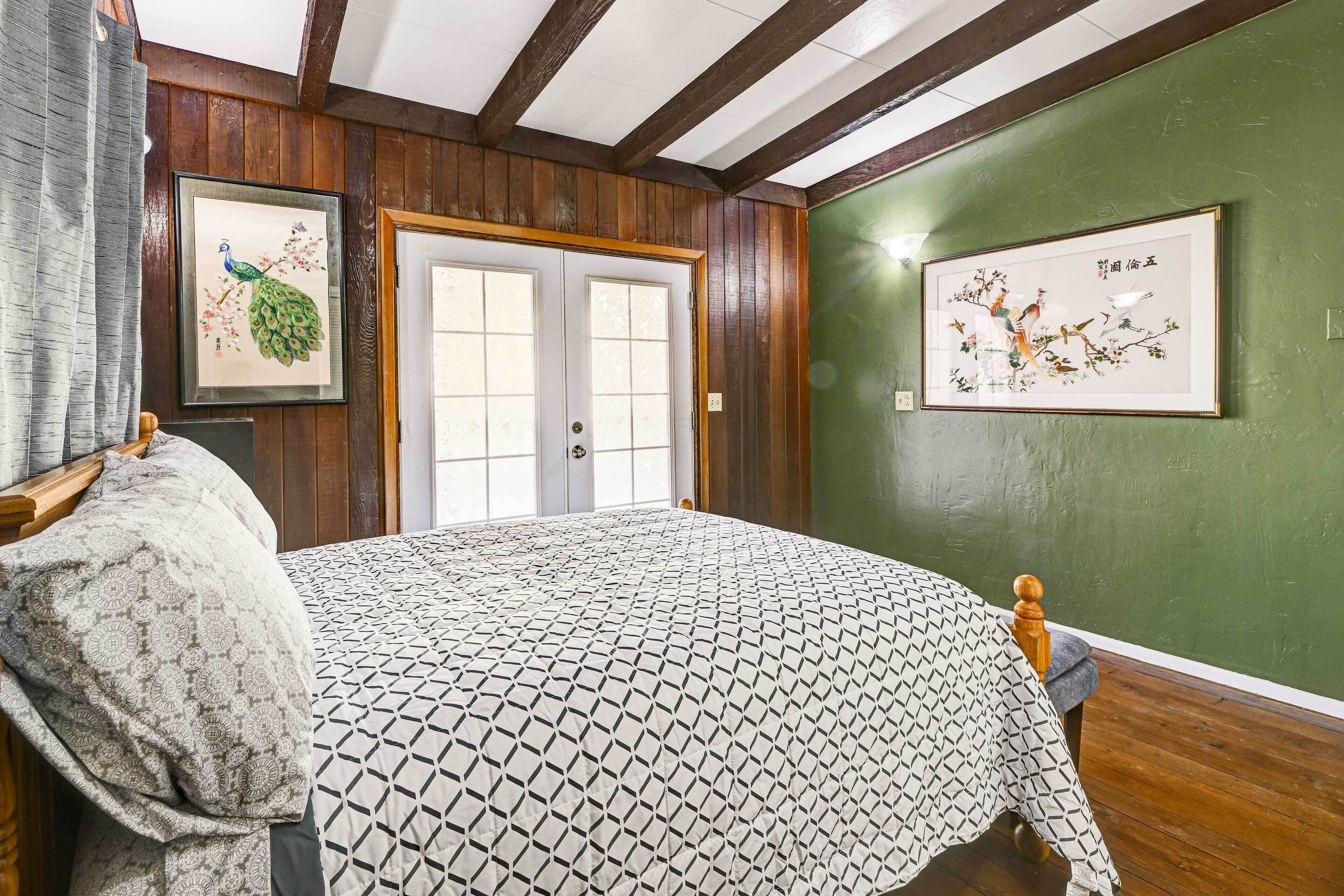A room with a bed, wooden walls, a green accent wall, and two framed artworks.
