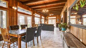 A spacious kitchen with wooden walls, a marble countertop, and a large dining area with chairs and a table.