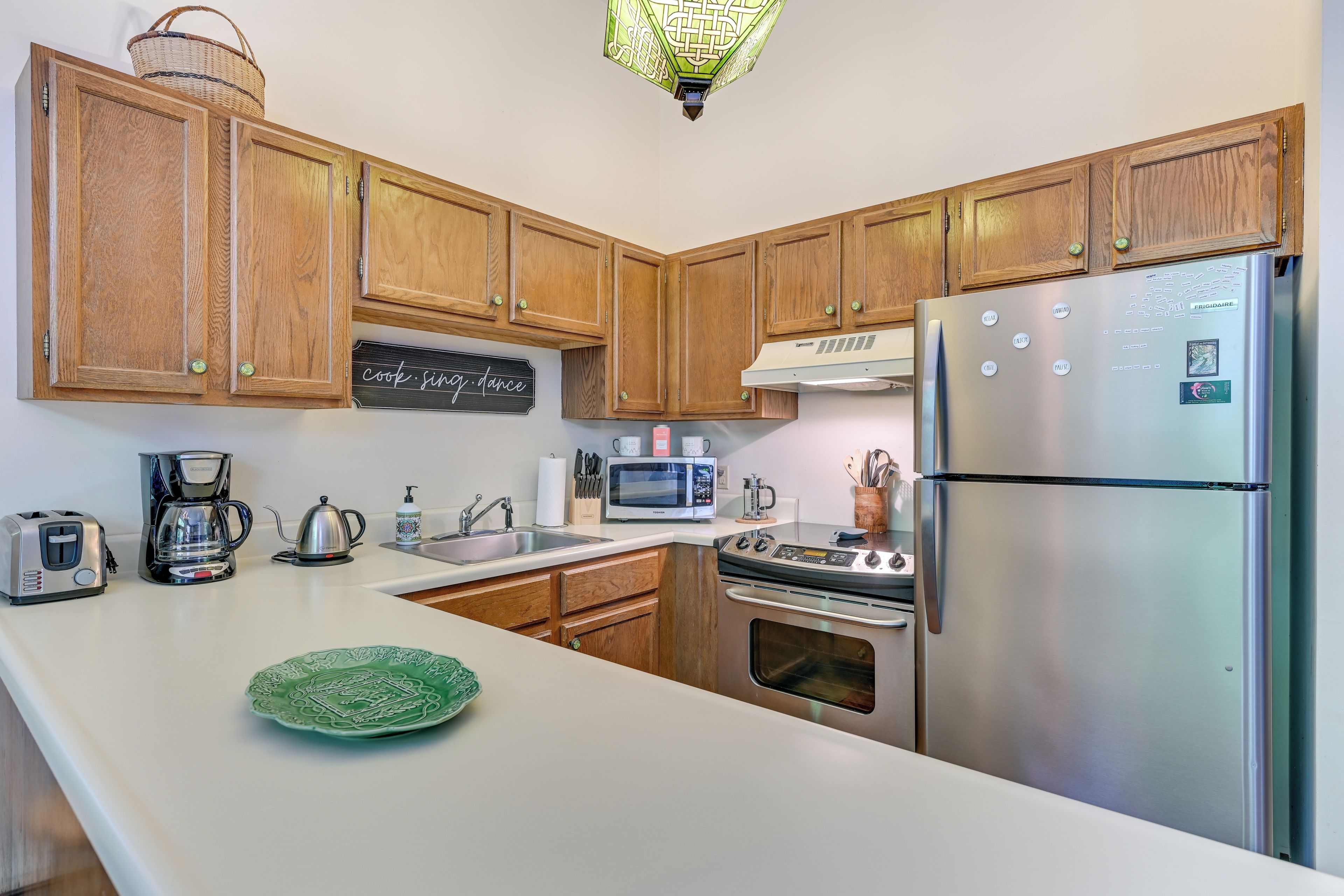 A kitchen with wooden cabinets, a stainless steel refrigerator, a microwave, a coffee maker, and a toaster.