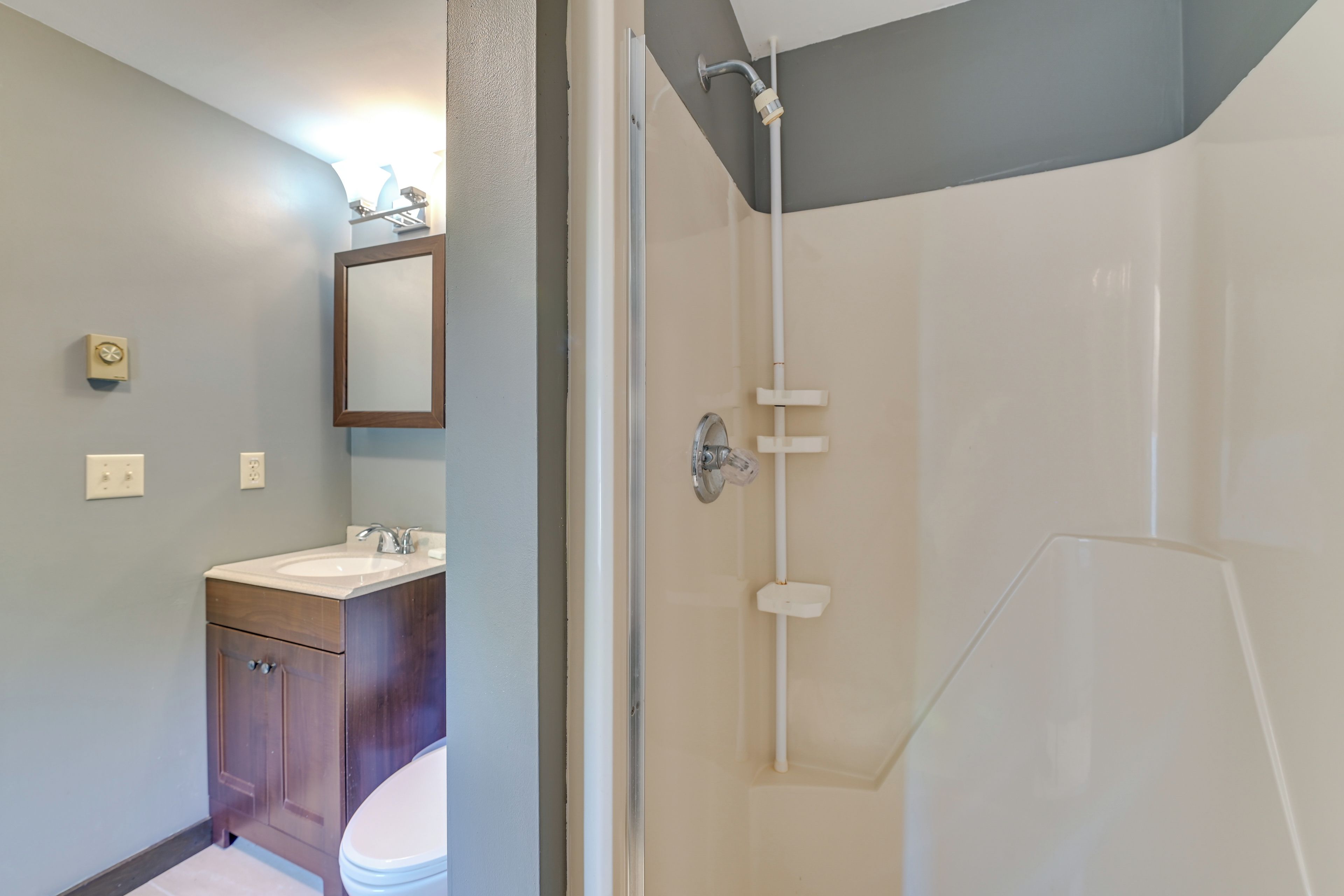 A bathroom with a shower, toilet, sink, and mirror.