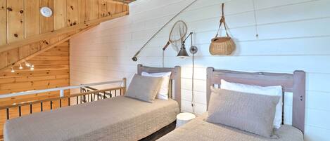 A bedroom with two beds, wooden ceiling beams, a sloped ceiling, and a hanging basket.