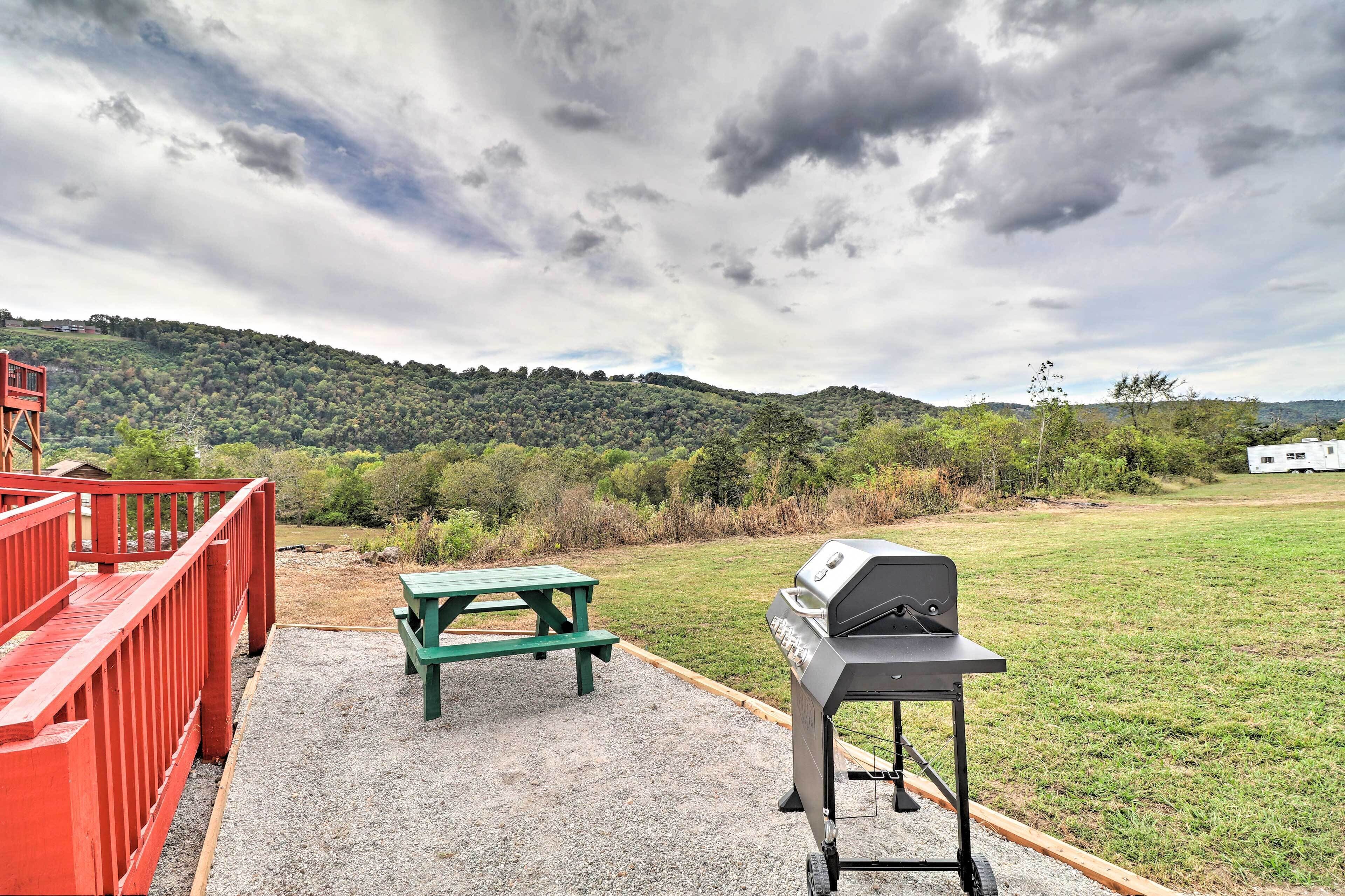 An outdoor area with a picnic table and a barbecue grill, surrounded by a red railing and a gravel path.