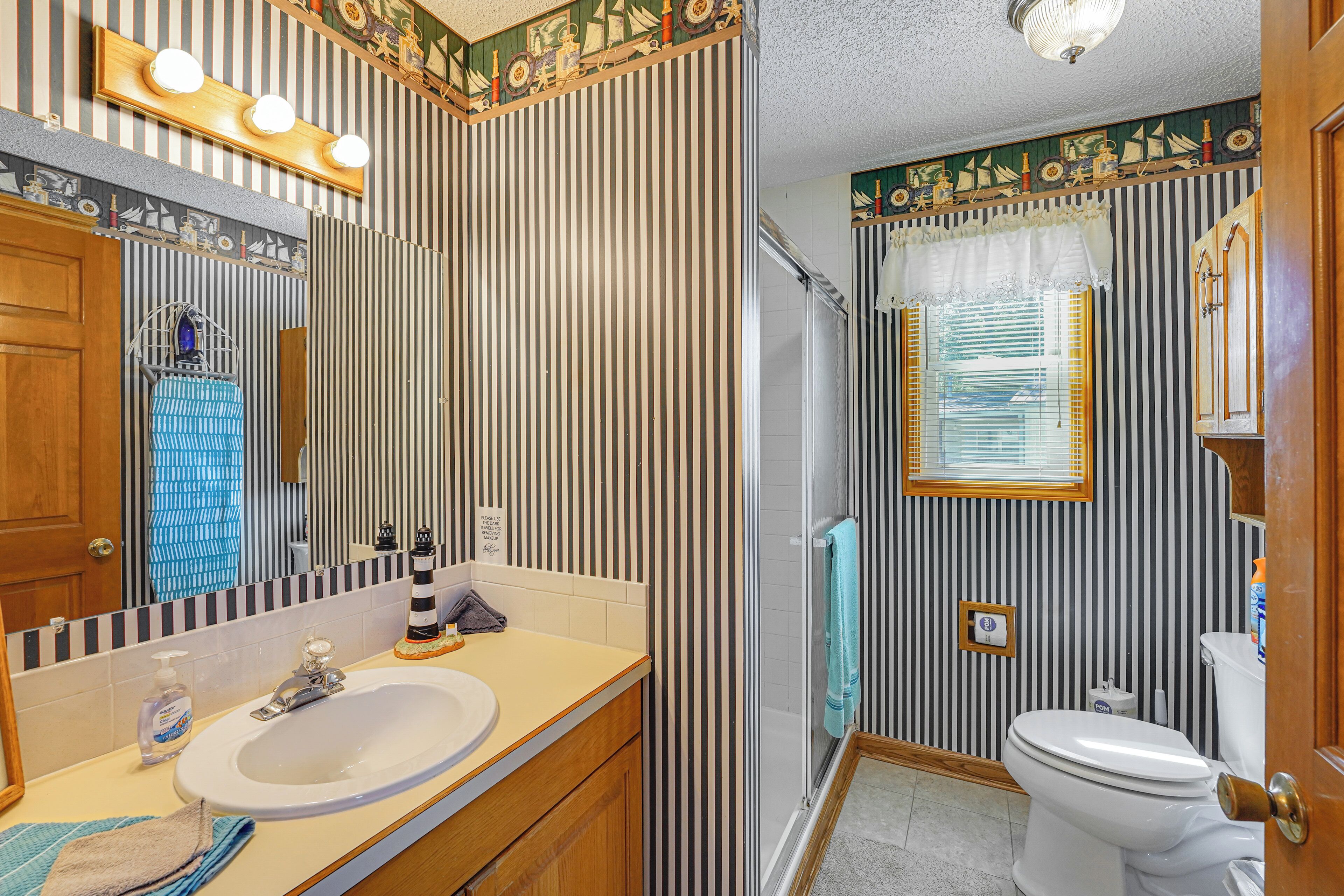 A bathroom with striped wallpaper, a sink, a mirror, a toilet, and a shower.
