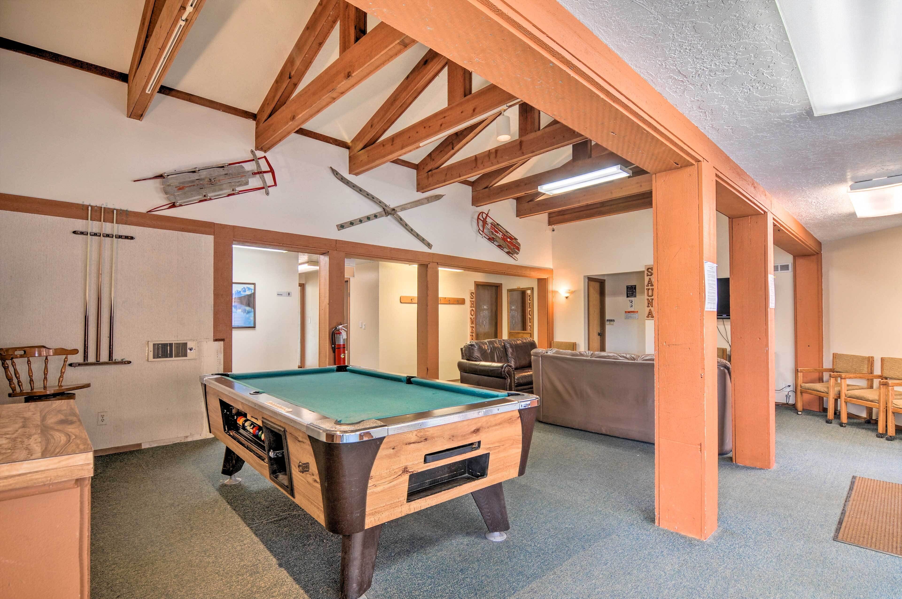 A pool table in a room with wooden beams, a fireplace, and a sofa.