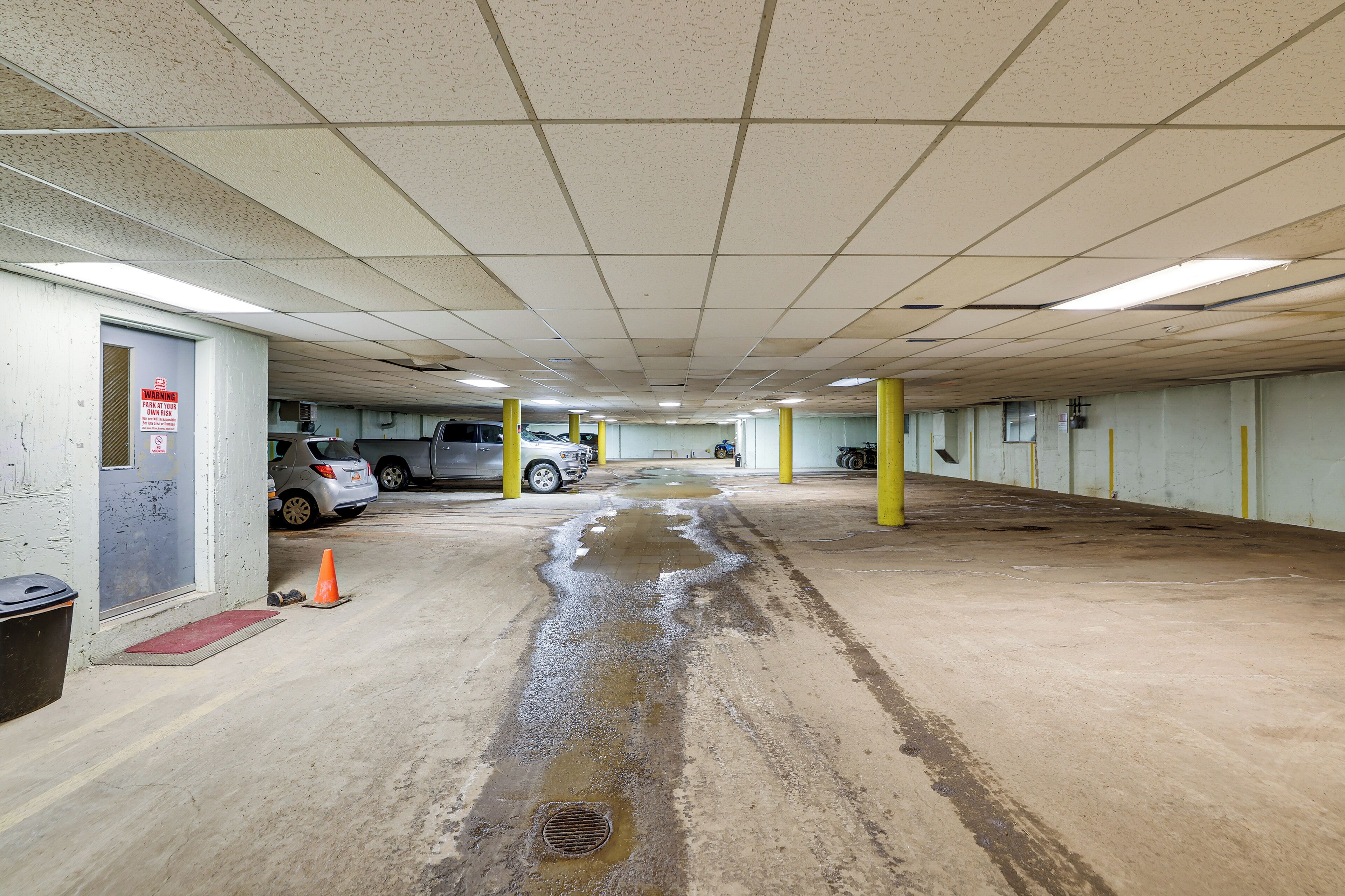 Een parkeergarage met betonnen vloeren, gele pilaren en een lekkage.