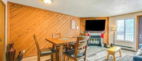 Un salon chaleureux avec un mur en bois, une cheminée, un téléviseur et un coin repas comprenant des chaises et une table.